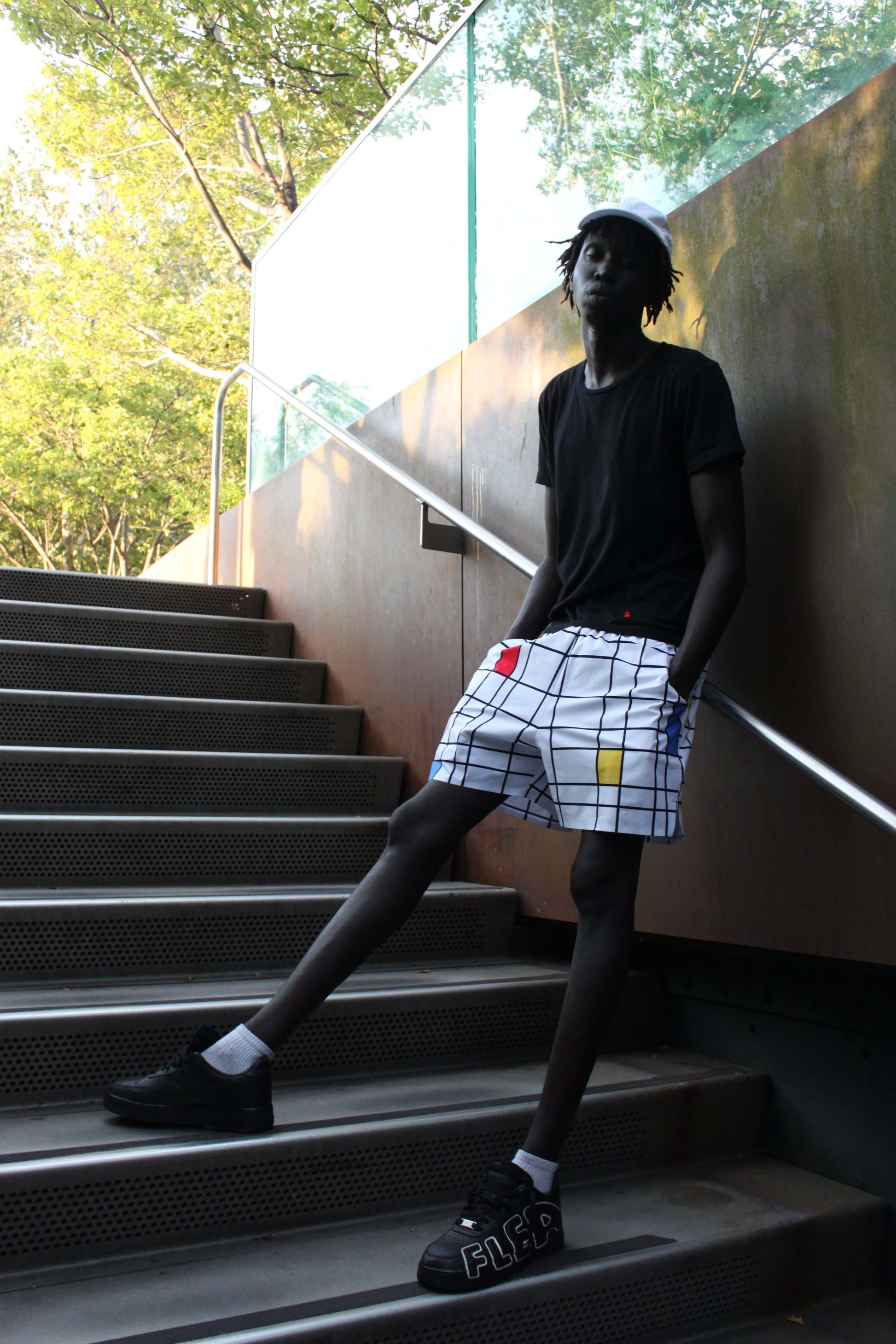 Man wearing Mondo Tennis Agnès lightweight technical shorts with a grid pattern and colored accents, standing on stairs outdoors